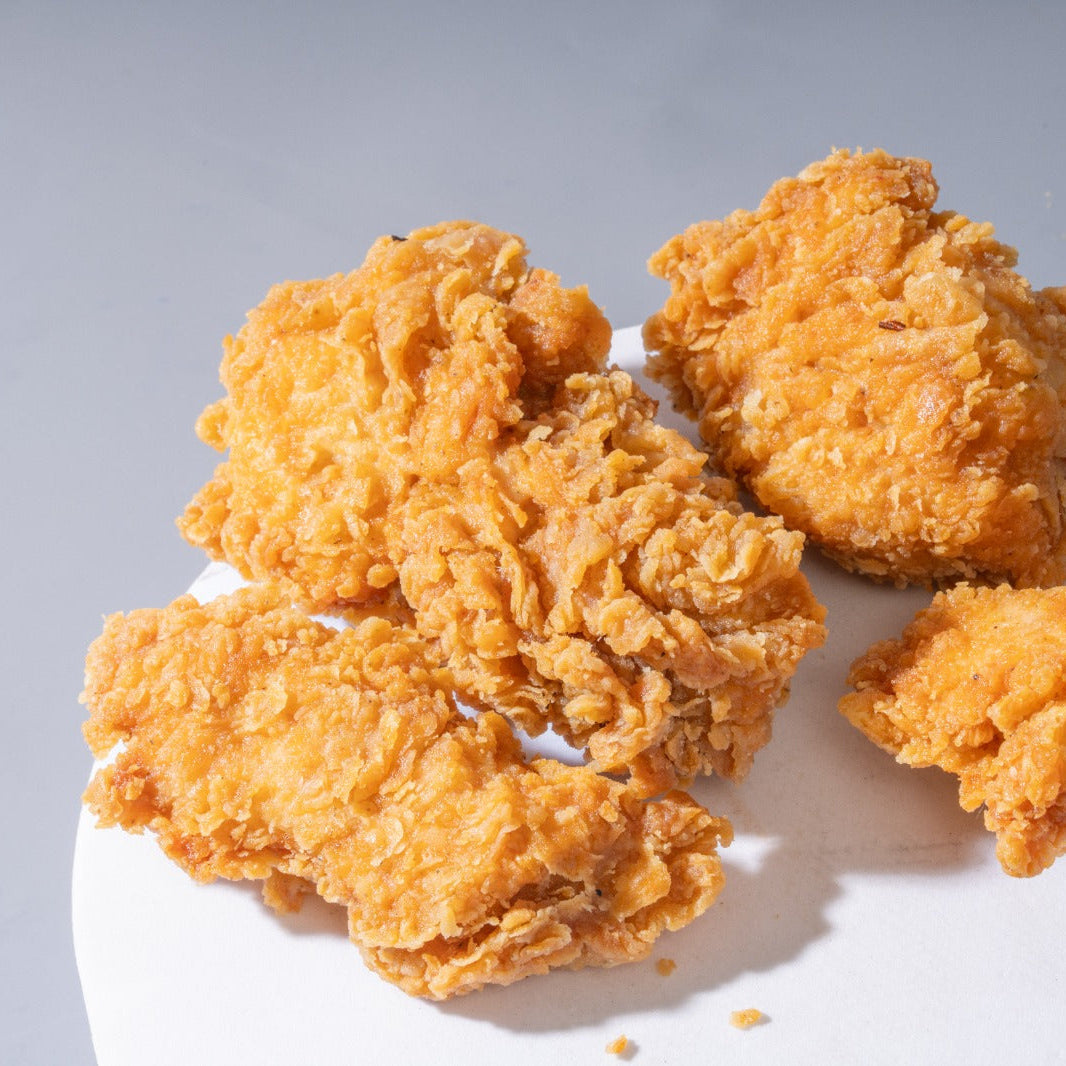Four golden-brown fried chicken nuggets with crispy, textured breading piled on a white plate against a light gray background.
